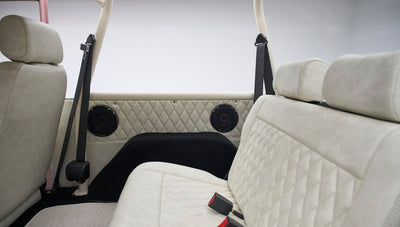 Rear diamond-stitched beige seats with black seat belts and speakers on side panels in a Classic Ford Bronco