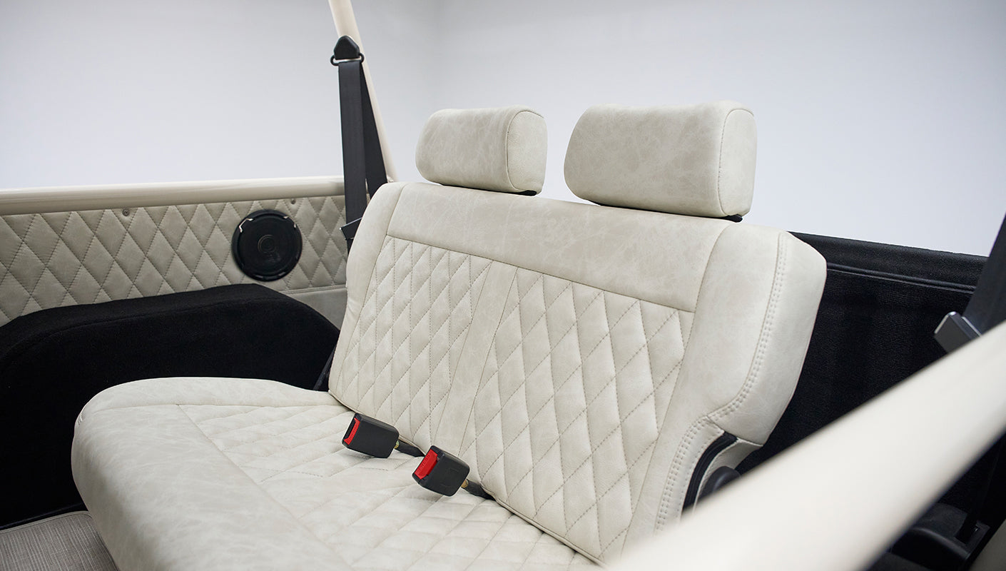 Back seat of a Classic Ford Bronco featuring beige diamond-stitched upholstery and black speaker panels