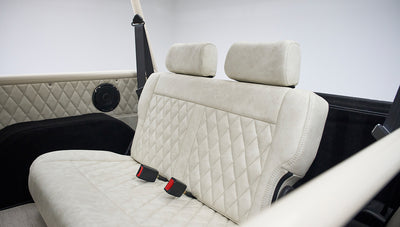 Back seat of a Classic Ford Bronco featuring beige diamond-stitched upholstery and black speaker panels