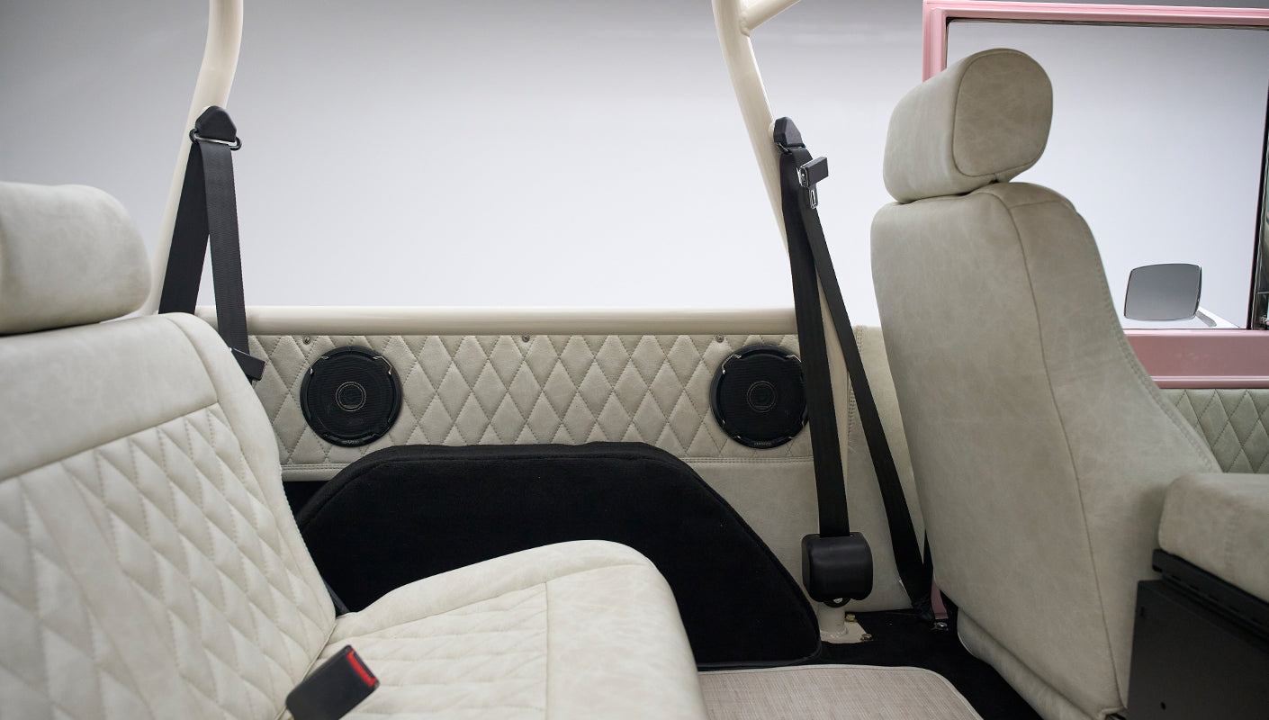 View of the rear seating area with beige diamond-stitched upholstery, black speaker panels, and safety belts in a Classic