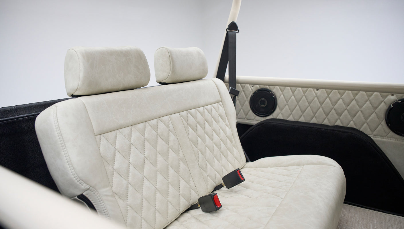 Close-up of rear bench with beige diamond-stitched upholstery and black seat belts inside a Classic Ford Bronco