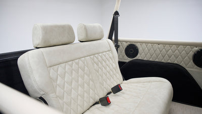 Close-up of rear bench with beige diamond-stitched upholstery and black seat belts inside a Classic Ford Bronco