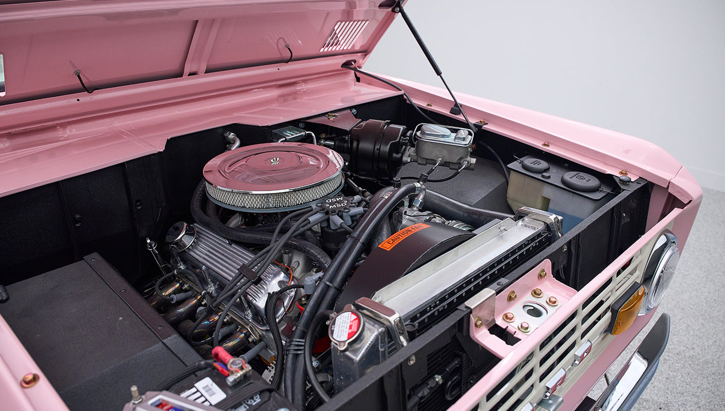 Engine compartment of a Classic Ford Bronco painted pink with hood open showing clean engine components