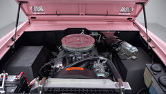 Front view into engine bay of a pink Classic Ford Bronco showing battery and air filter under open hood