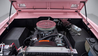 Front view into engine bay of a pink Classic Ford Bronco showing battery and air filter under open hood