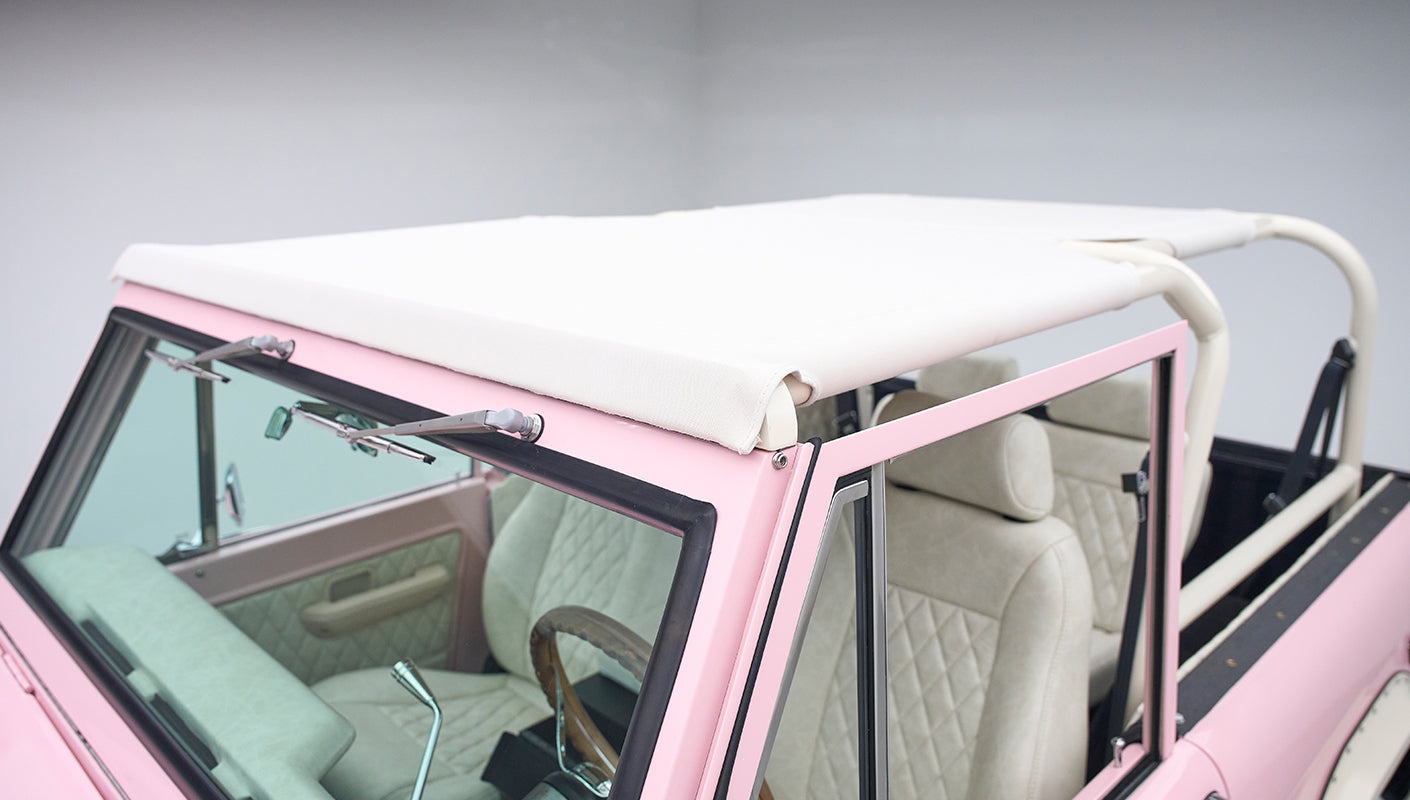 Interior view of pink Classic Ford Bronco with white soft top and cream upholstery