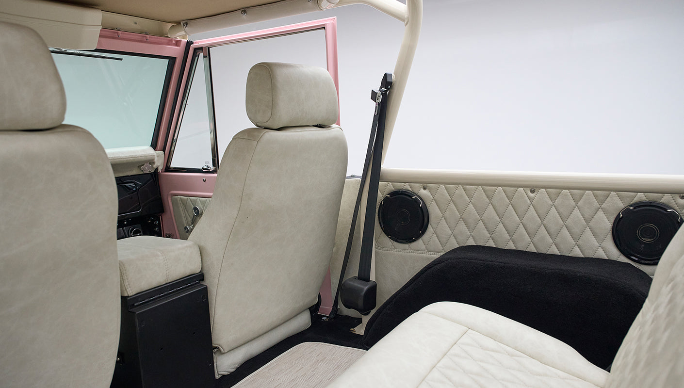 Interior view of a Classic Ford Bronco showcasing cream seats, speaker, and seatbelt detail.