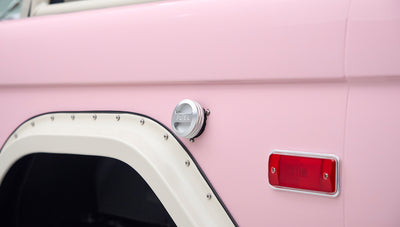 Pink Classic Ford Bronco side panel with white fender flares and a silver fuel cap visible.
