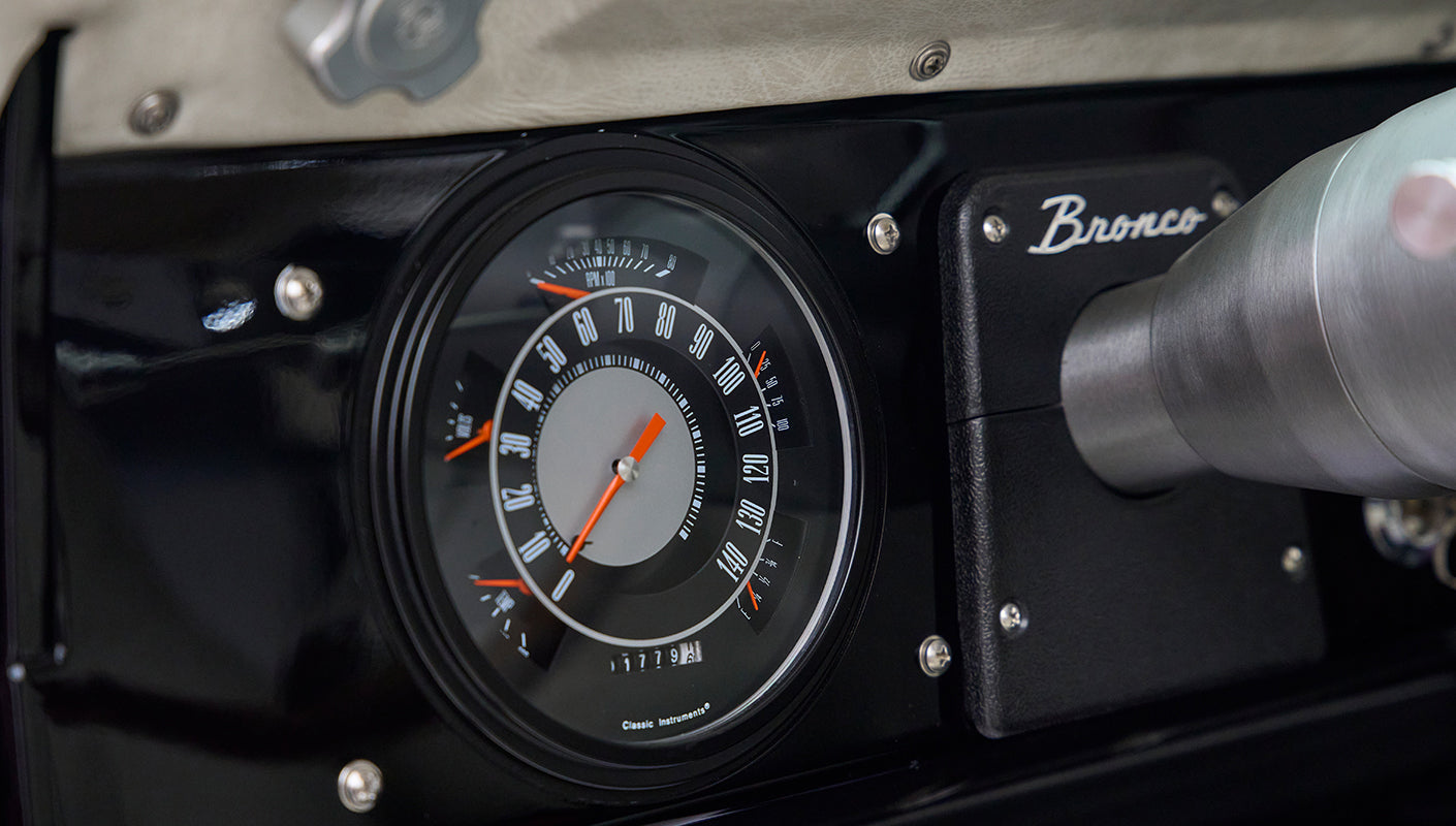 Close-up of Classic Ford Bronco dashboard showing round speedometer with black background.