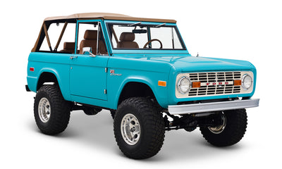 Classic Ford Bronco in peacock blue with tan soft top, lifted suspension, and off-road tires.