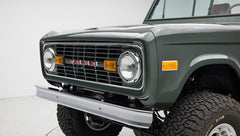Close-up of Classic Ford Bronco front grill showing round headlights and dark green paint.