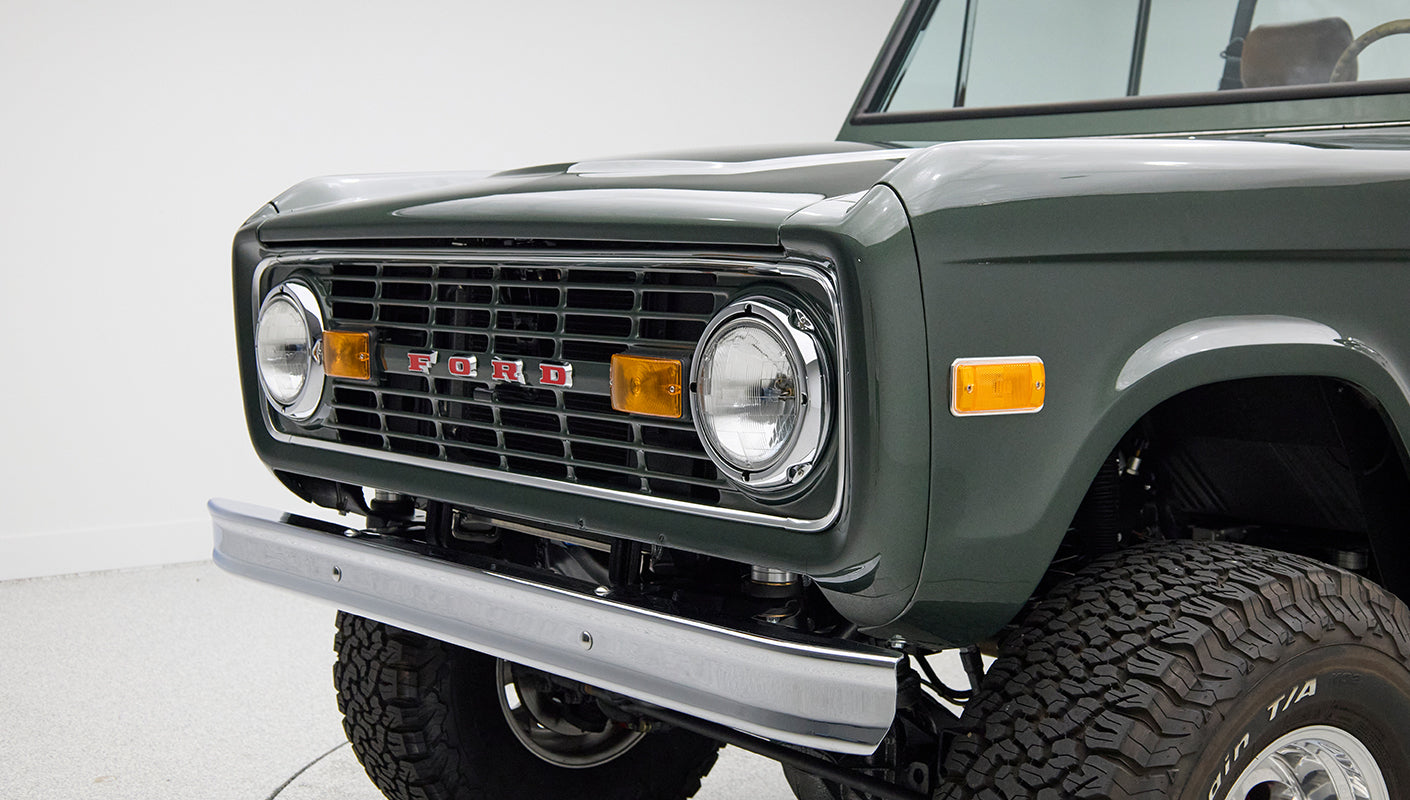 Close-up of Classic Ford Bronco front grill showing round headlights and dark green paint.