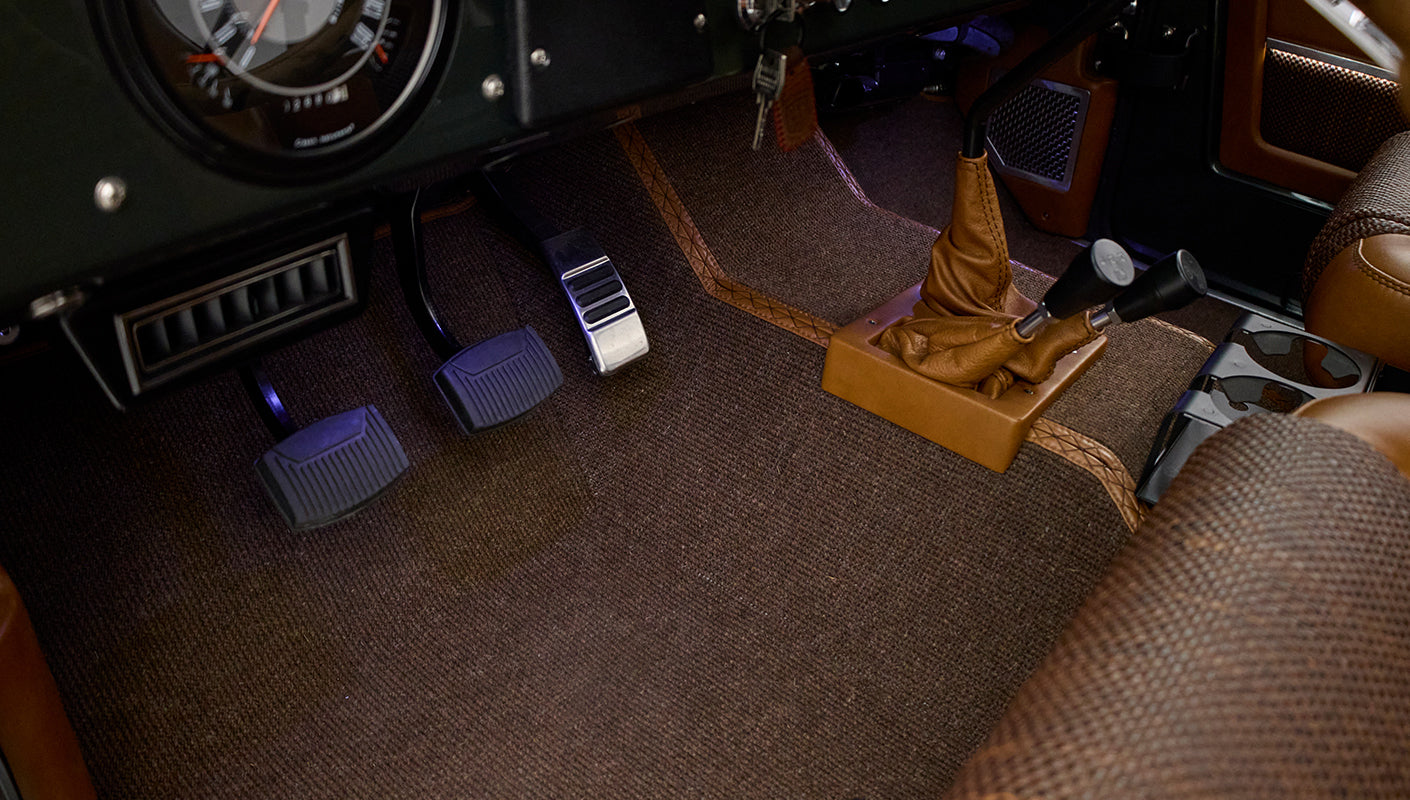 Classic Ford Bronco interior floor showing pedals and brown carpet with leather-wrapped gear shifters