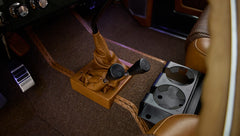 Classic Ford Bronco gear levers wrapped in brown leather beside black plastic dual cup holders on carpeted floor
