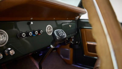 Manual transmission gear shift stick near Classic Ford Bronco dashboard with knobs and switches