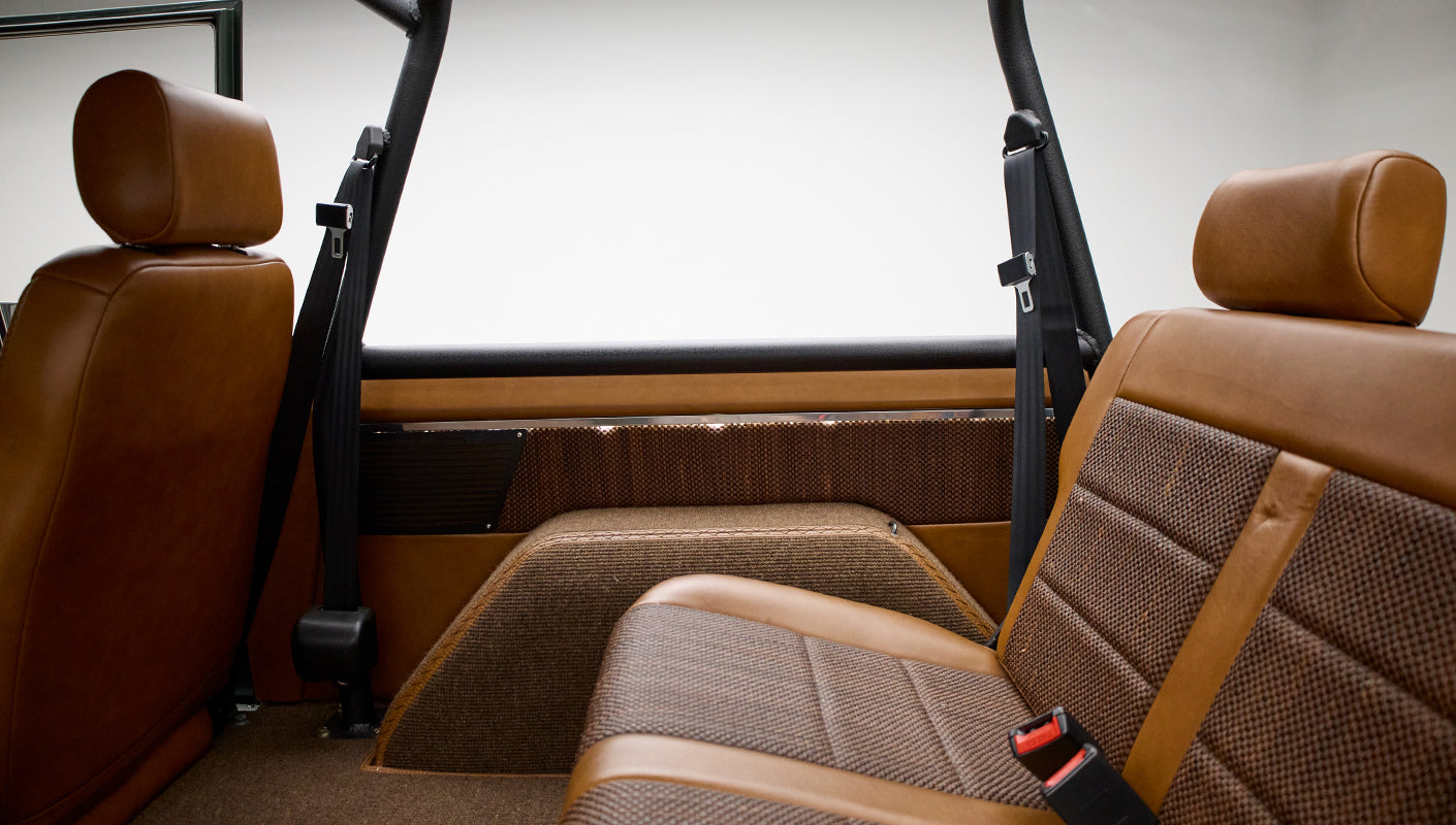 Rear seats inside Classic Ford Bronco with brown leather and woven fabric upholstery and safety harness bars