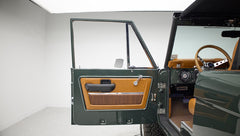 Open door showing dark green exterior and tan interior with woven insert on Classic Ford Bronco
