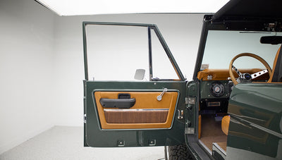 Open door showing dark green exterior and tan interior with woven insert on Classic Ford Bronco