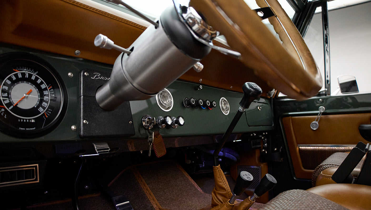 Full dashboard and steering wheel with gear levers and tan upholstery inside Classic Ford Bronco