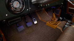 Pedals and multiple gearshift levers on brown carpet floor inside Classic Ford Bronco