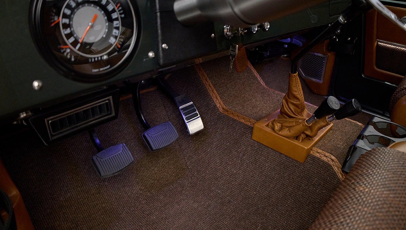 Pedals and multiple gearshift levers on brown carpet floor inside Classic Ford Bronco