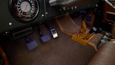 Pedals and multiple gearshift levers on brown carpet floor inside Classic Ford Bronco