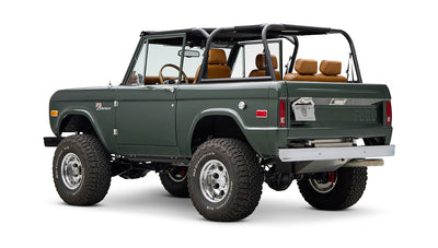 Classic Ford Bronco in dark green with tan leather interior, viewed from rear left side with open top.