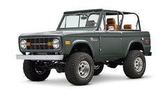 Classic Ford Bronco dark green front left angled view with round headlights and open roof.