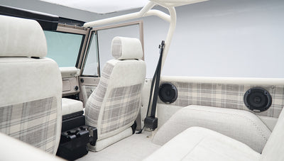 Interior side and rear view of classic Ford Bronco showing plaid seat upholstery and speakers