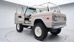 Rear exterior view of classic Ford Bronco with open driver door, white wheels, and beige body
