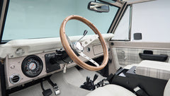 Dashboard, wood steering wheel, and front seats with plaid accents in classic Ford Bronco interior
