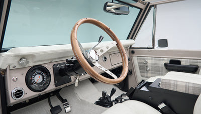 Dashboard, wood steering wheel, and front seats with plaid accents in classic Ford Bronco interior