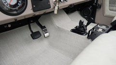 Pedals, manual gear levers, and light gray carpeted floor in classic Ford Bronco driver area