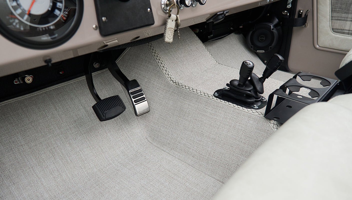 Pedals, manual gear levers, and light gray carpeted floor in classic Ford Bronco driver area