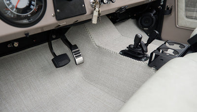 Pedals, manual gear levers, and light gray carpeted floor in classic Ford Bronco driver area