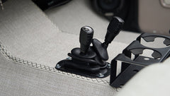 Close-up of two black gear shift levers and a cup holder on carpeted floor of classic Ford Bronco