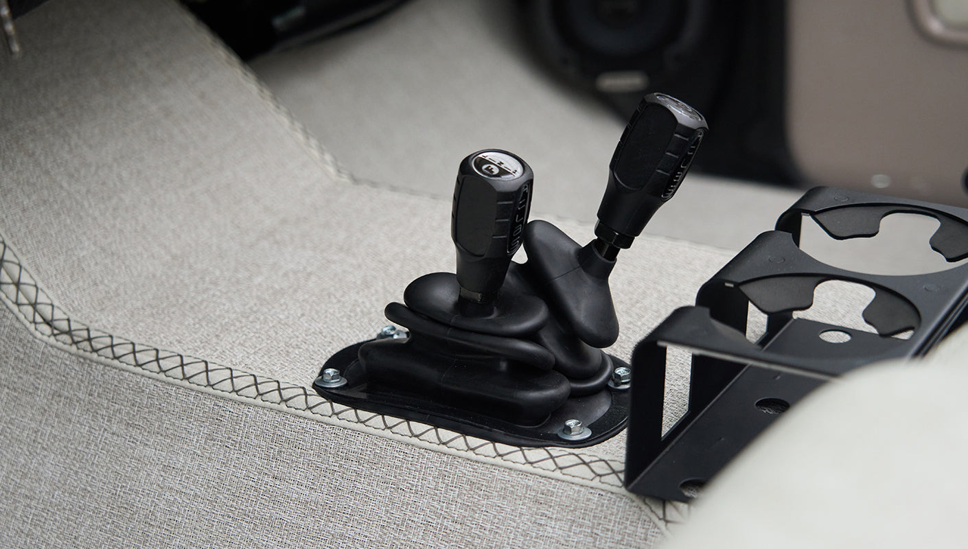 Close-up of two black gear shift levers and a cup holder on carpeted floor of classic Ford Bronco