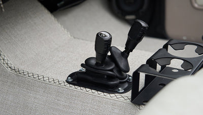 Close-up of two black gear shift levers and a cup holder on carpeted floor of classic Ford Bronco