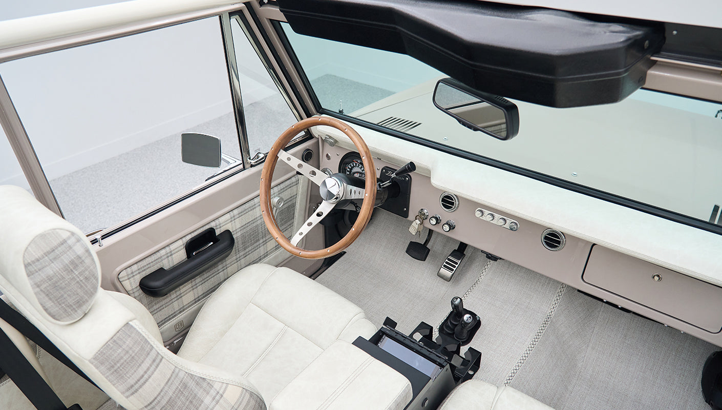Interior view of Classic Ford Bronco showing steering wheel, dashboard, and seats in light tones