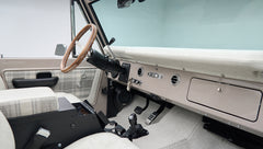 Classic Ford Bronco dashboard with wood steering wheel, vents, and plaid seat