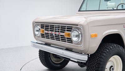 Front corner close-up of a Classic Ford Bronco in dove gray highlighting the grille and tire