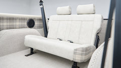 Rear seating area inside Classic Ford Bronco with cream and plaid upholstery and roll cage