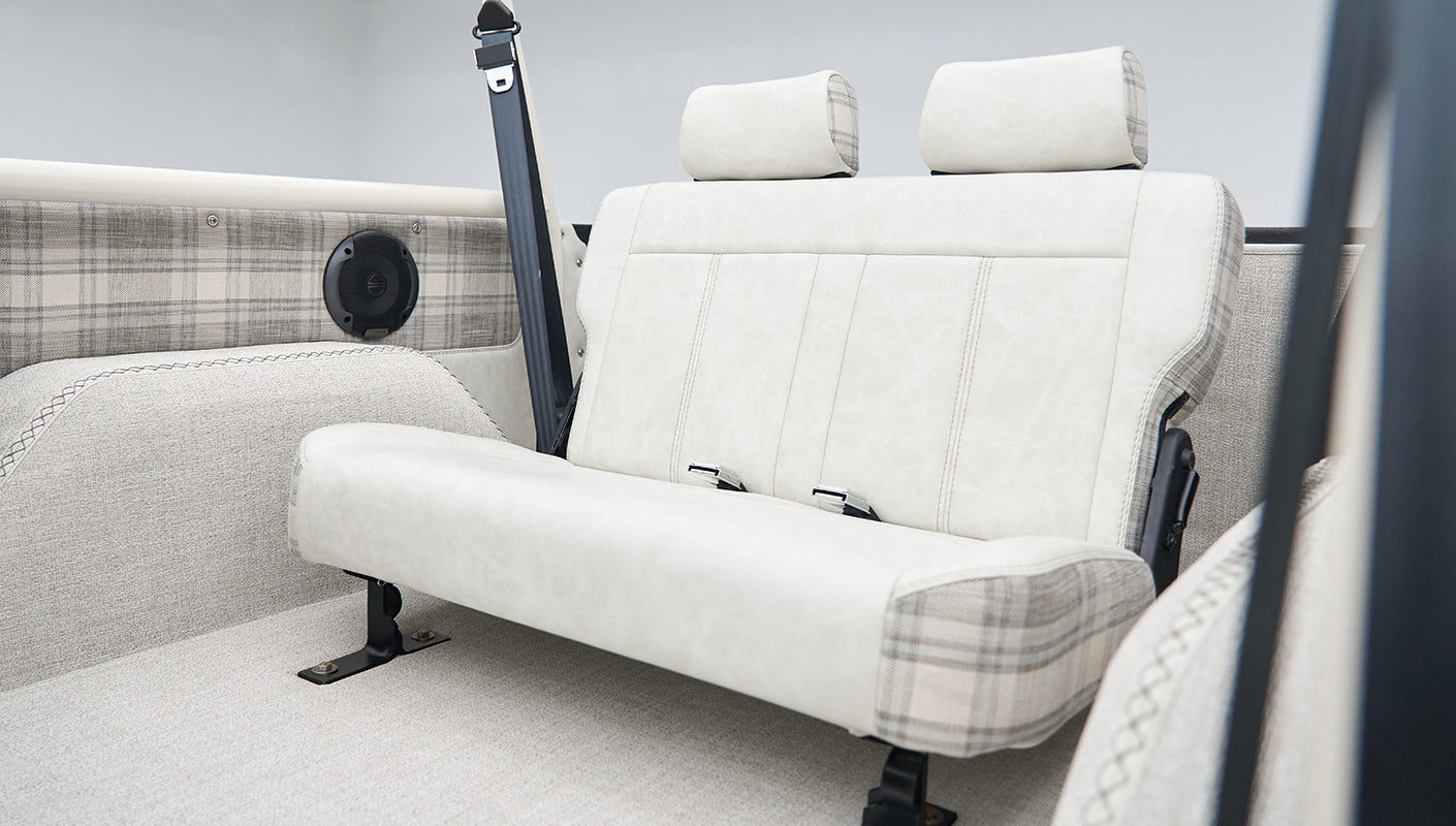 Rear seating area inside Classic Ford Bronco with cream and plaid upholstery and roll cage