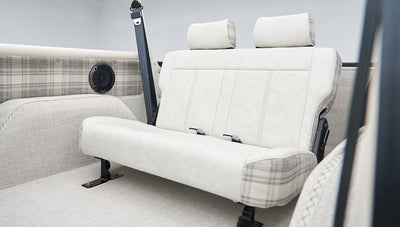 Rear seating area inside Classic Ford Bronco with cream and plaid upholstery and roll cage