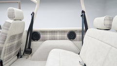 Partial view of front and rear seats with plaid upholstery and black seat belts in classic Ford Bronco