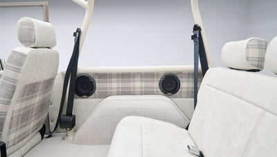Partial view of front and rear seats with plaid upholstery and black seat belts in classic Ford Bronco