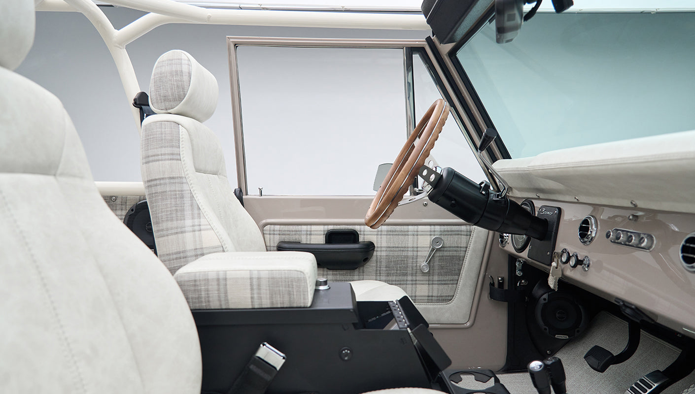 Driver side interior of Classic Ford Bronco with plaid seats, steering wheel, and door panel