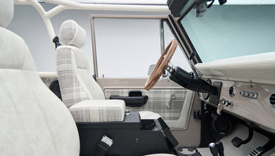 Driver side interior of Classic Ford Bronco with plaid seats, steering wheel, and door panel