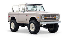 Classic Ford Bronco in dove gray, white wheels, front driver side angle view showing interior seats