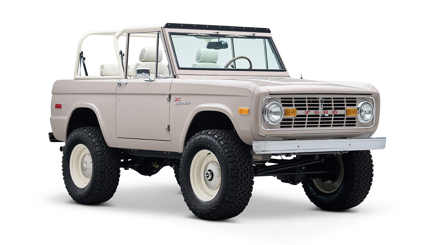 Classic Ford Bronco in dove gray, white wheels, front driver side angle view showing interior seats